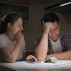 Short on Cash image of man and woman frustrated with hands on their head and bills and small amount of cash on table